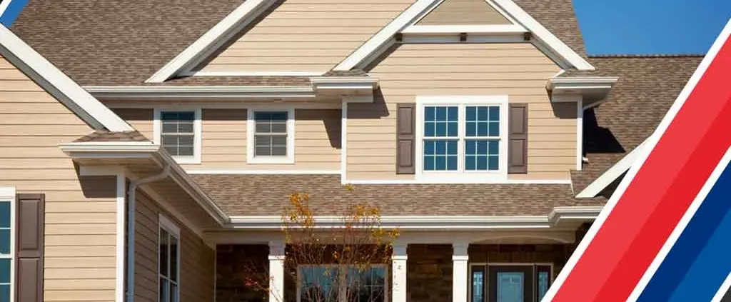 Elegant suburban home with beige siding and brown roof against a clear blue sky. Decorative red, white, and blue stripes on the right.