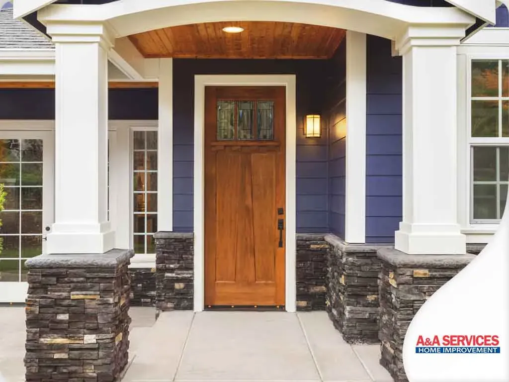 Front entrance of a house with a wooden door, framed by white pillars and stone walls. Blue siding and a warm light create a welcoming ambiance.