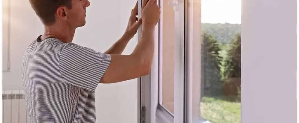 A person in a striped shirt installs a window seal in a sunlit room, emphasizing focus and precision. Outside, trees are visible, suggesting a serene setting.