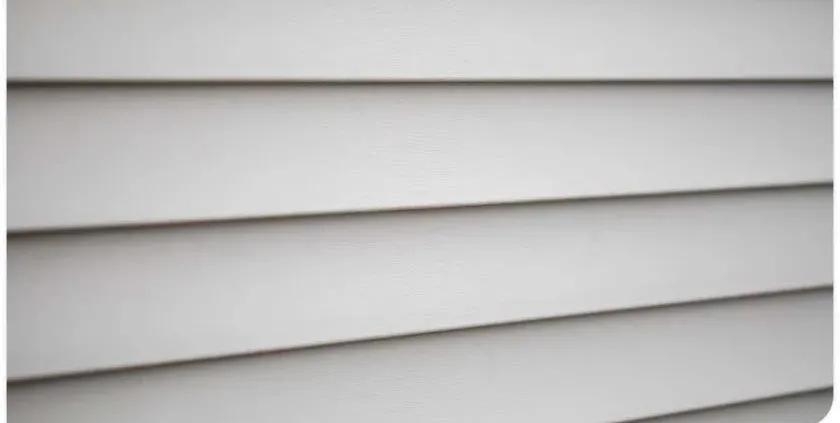 Close-up of light gray, horizontal vinyl siding. The smooth panels overlap slightly, creating clean, parallel lines. The tone is neutral and uniform.