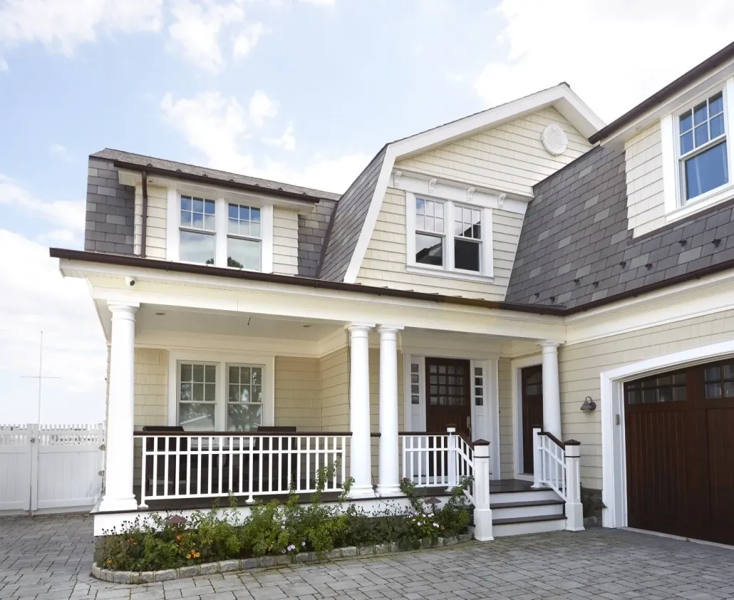 Two-story house with a charming porch, white railings, and columns. Cream siding and gray roof shingles evoke a welcoming and cozy atmosphere.