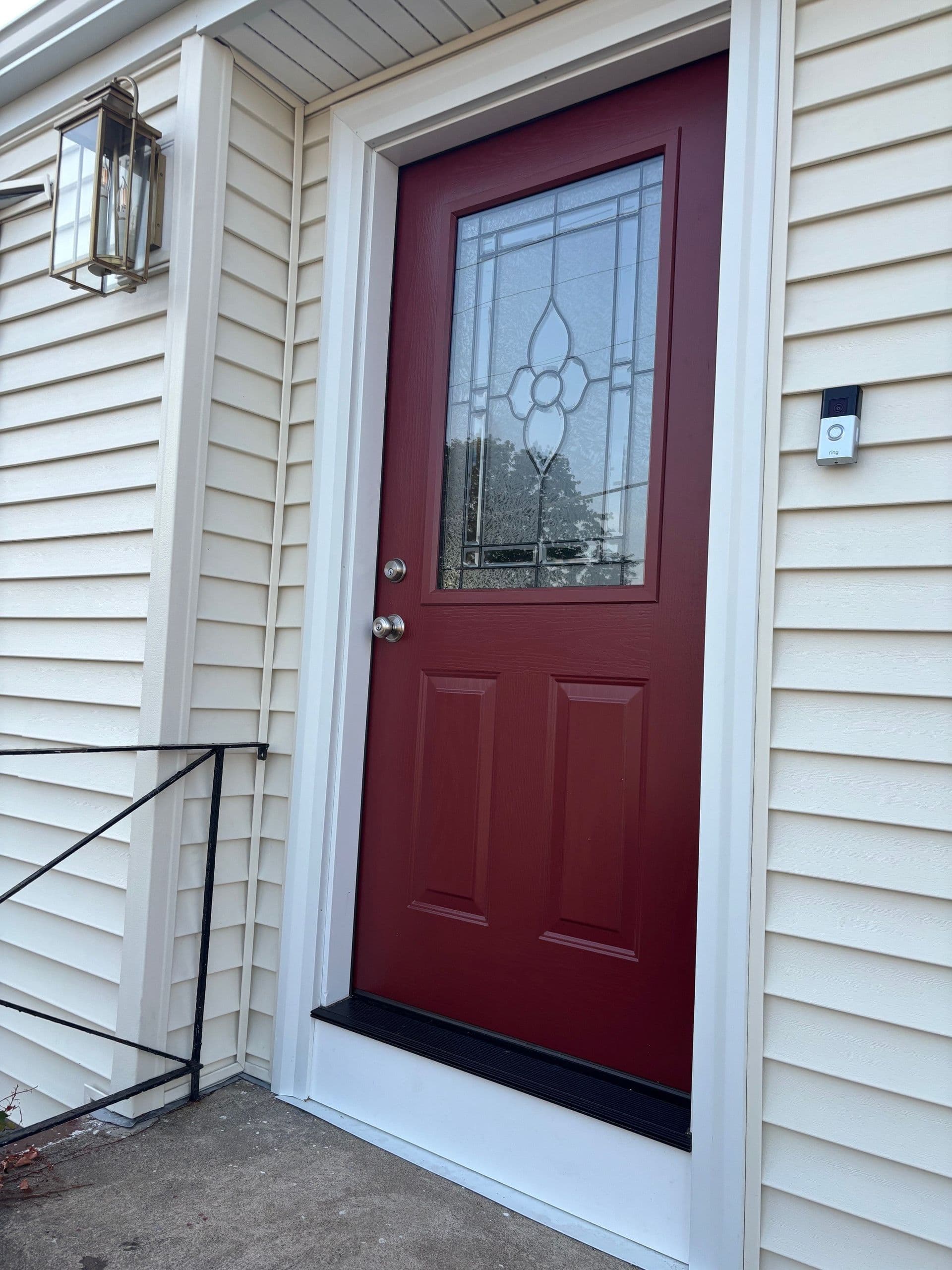 Red door with decorative glass panel on a beige house, flanked by a lantern-style light fixture and a doorbell. The scene conveys a welcoming entrance.