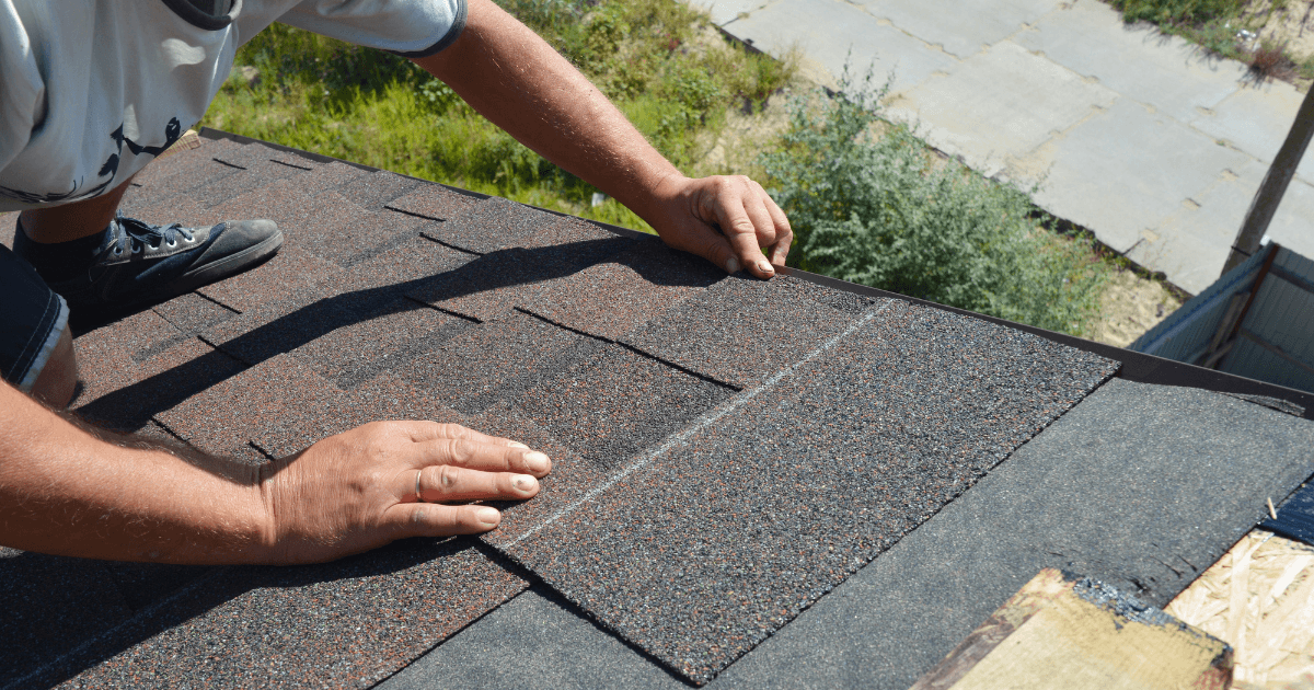 A person installing new shingles on a roof under bright sunlight.