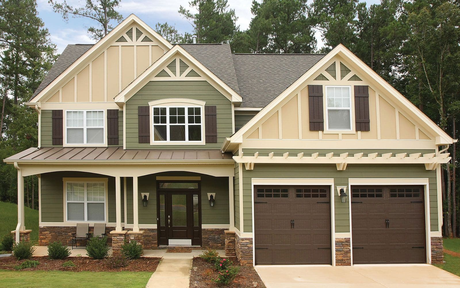 A large two-story house with green siding, tan gables with white trim, dark brown shutters, and a two-car garage.