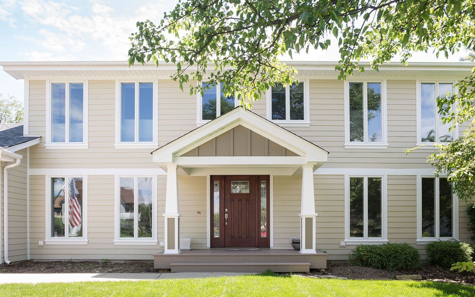 A beige two-story house with a prominent dark wood front door and a gabled porch supported by white columns.