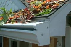 Gutter filled with autumn leaves on a sloped roof. The scene conveys a need for seasonal cleaning, with vibrant red and orange tones.