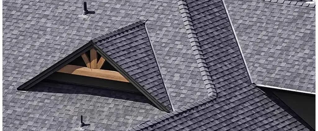 Aerial view of a gray shingled roof with intersecting pitches and a triangular dormer. The clean lines and neat shingles convey a sense of order and precision.