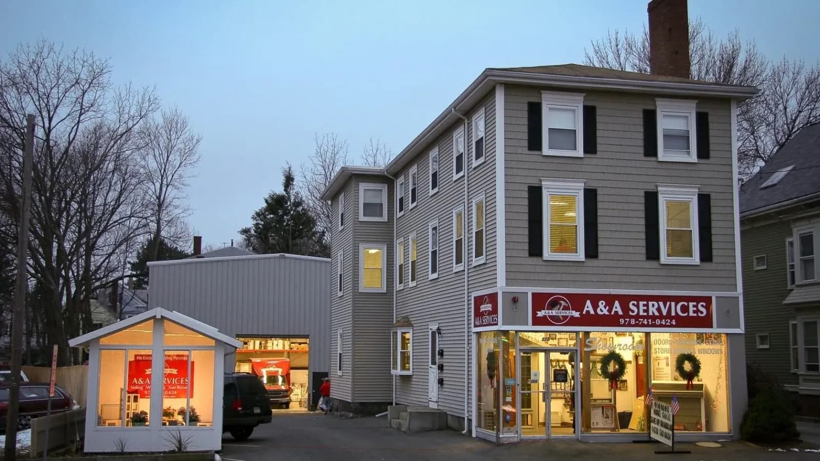 Three-story building at dusk houses A&A Services. Warm lights inside, red sign outside; festive wreaths on doors suggest a welcoming, cozy atmosphere.