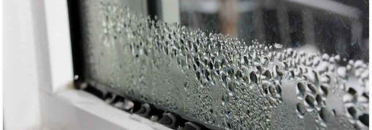 Condensation droplets densely cover a window pane, creating a textured pattern against a blurred background, suggesting a cold, humid atmosphere.
