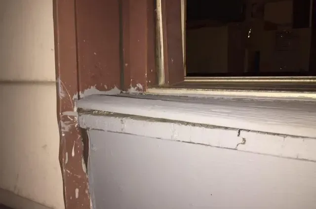 Close-up of a poorly painted window frame, showing peeling white paint on the sill and mismatched brown paint on the side, conveying a sense of neglect.